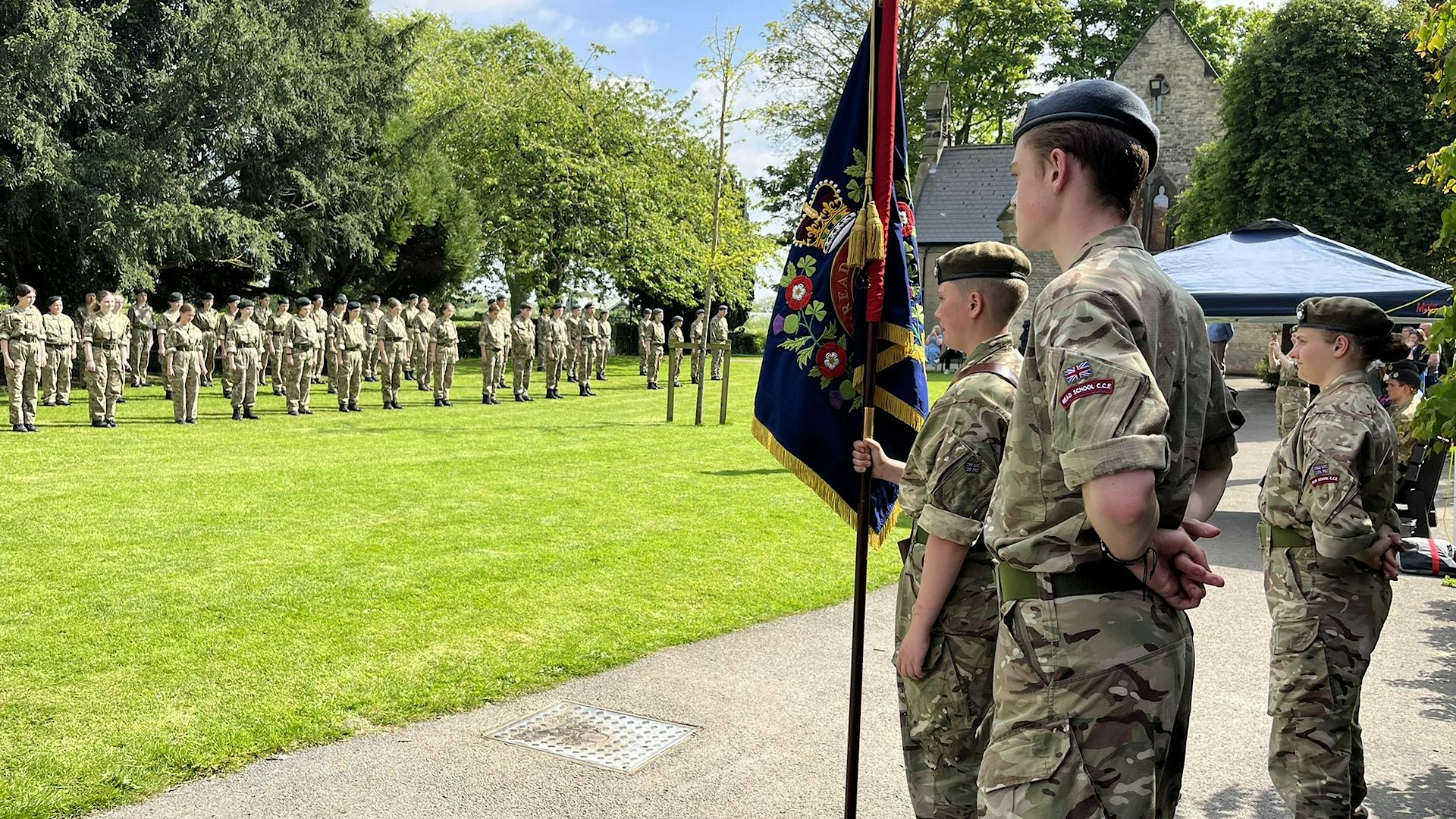 Cadets holding school flag in the forefront with cadets lining up in the background
